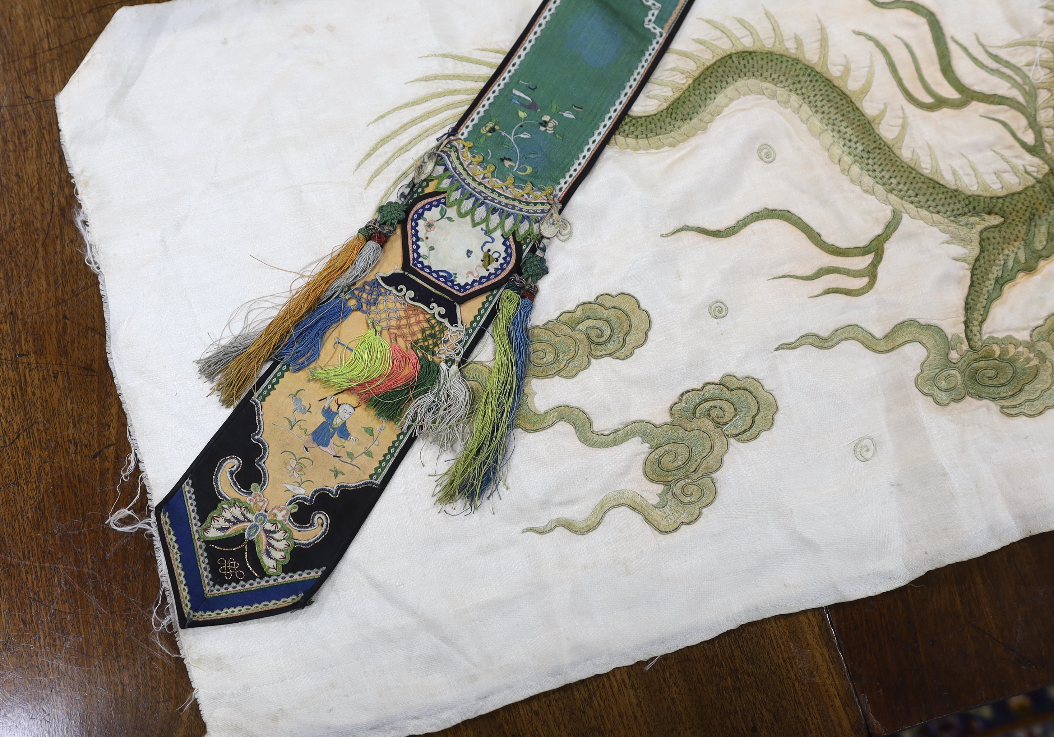 A collection of Chinese embroideries, to include a pair of tasselled embroidered panels to a wedding skirt, two pairs of Chinese children's shoes, a pair of embroidered sleeve bands, a panel of gauze of polychrome silk a